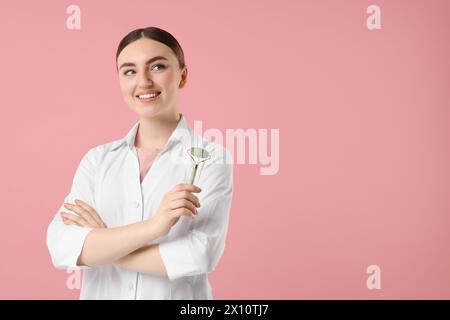 Cosmétologue avec rouleau facial sur fond rose, espace pour le texte Banque D'Images