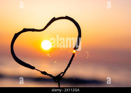 Étincelant en forme de coeur brûlant sur fond de mer et soleil levant à l'aube. Feu du Bengale en forme de coeur scintillant à l'aube du lever du soleil et au coucher du soleil sur la mer. Amour engouement Saint-Valentin Banque D'Images