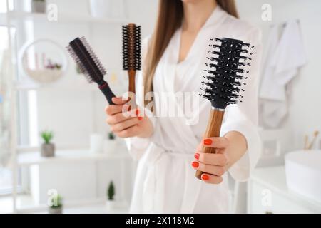 Belle jeune femme avec brosse à cheveux ronde dans la salle de bain, gros plan Banque D'Images