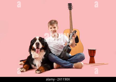 Petit garçon avec chien de montagne bernois et instruments de musique sur fond rose Banque D'Images