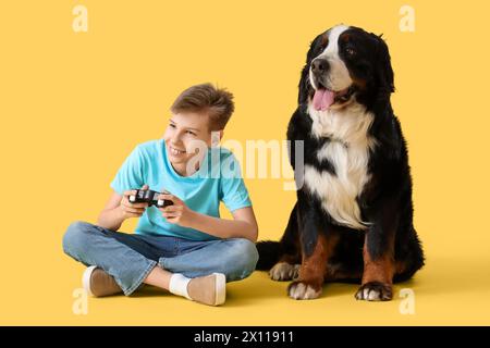 Petit garçon avec chien de montagne bernois jouant au jeu vidéo sur fond jaune Banque D'Images