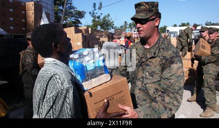 Un Marine du bataillon de logistique de combat 22, 22e unité expéditionnaire des Marines, aide un Haïtien à ramasser une caisse de repas prêts-à-manger et d'eau embouteillée sur un site de distribution d'aide humanitaire à petit Goave, Haïti, 28 janvier 2010. Banque D'Images