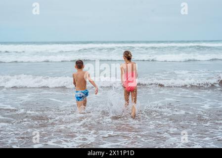 Frères et sœurs jouant sur la plage, courir, sauter, s'amuser sur la plage de sable des îles Canaries. Concept de vacances d'été à la plage familiale avec enfants. Banque D'Images