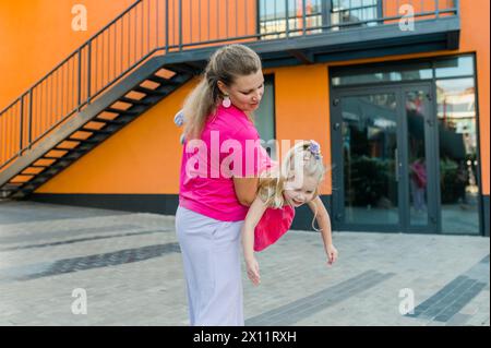 Heureuse mère balançant et filant fille mignonne en cercles par les bras à l'extérieur. Gamin ludique énergique et joyeux s'amusant tout en se liant à maman Banque D'Images