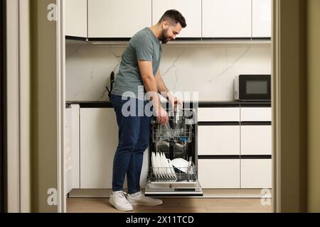 Homme souriant chargeant le lave-vaisselle avec des verres dans la cuisine Banque D'Images