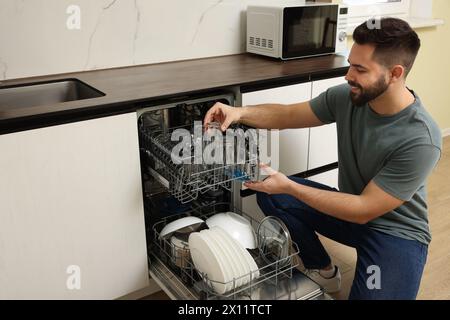 Homme souriant chargeant le lave-vaisselle avec des verres dans la cuisine Banque D'Images