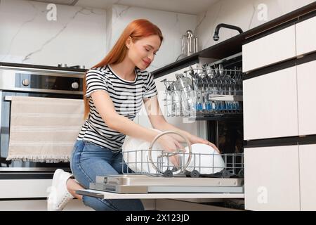 Femme chargeant le lave-vaisselle avec des assiettes dans la cuisine Banque D'Images