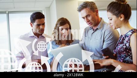 Image de flèches autour des icônes du globe au-dessus de divers collègues discutant des rapports sur l'ordinateur portable au bureau Banque D'Images