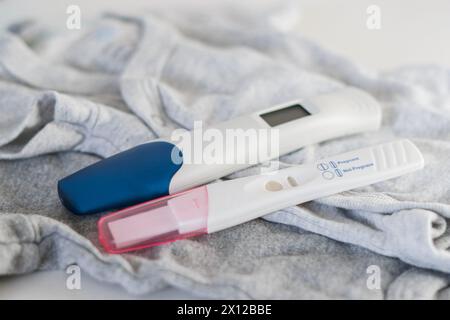 Gros plan de deux tests de grossesse positifs sur des vêtements de bébé Banque D'Images