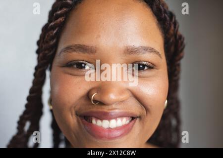 Jeune femme biraciale avec des cheveux tressés sourit à la caméra dans un bureau d'affaires moderne Banque D'Images