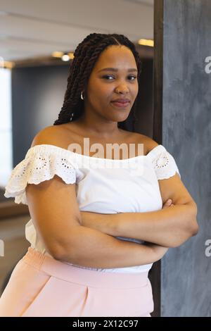 Jeune femme biraciale debout avec les bras croisés dans un bureau d'affaires moderne Banque D'Images