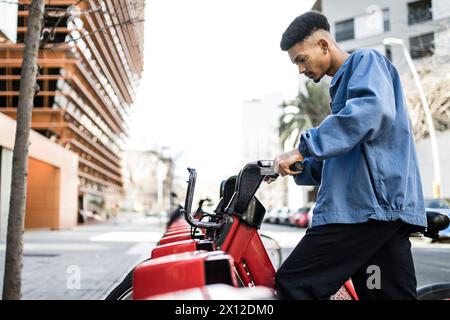 Jeune adulte tenant un vélo rouge dans la rue. Banque D'Images