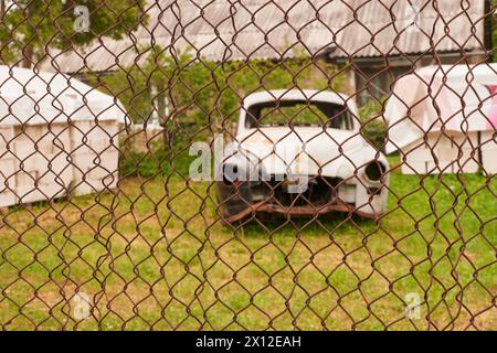 Ein teilweise zerlegtes historisches Auto steht in einem Garten hinter einen Zaun Banque D'Images