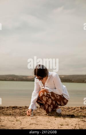 Fille dans une chemise blanche et lunettes de soleil à côté d'un beau lac Banque D'Images