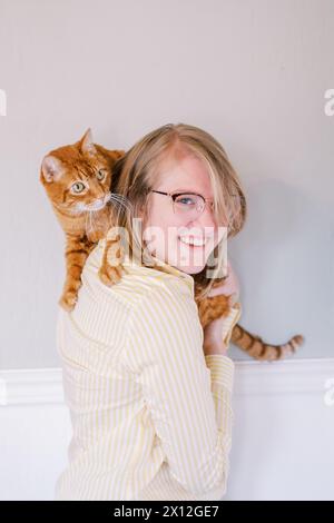 Femme joyeuse avec chat au gingembre sur l'épaule à l'intérieur Banque D'Images