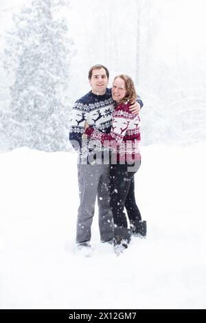 Couple souriant en chandails de Noël dans la neige Banque D'Images