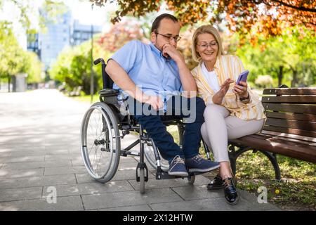 L'homme en fauteuil roulant passe du temps avec sa mère dans le parc. Banque D'Images