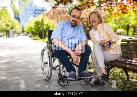 L'homme en fauteuil roulant passe du temps avec sa mère dans le parc. Banque D'Images