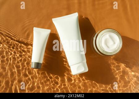 Tubes et pot avec crème hydratante dans l'eau sur fond orange, vue de dessus Banque D'Images