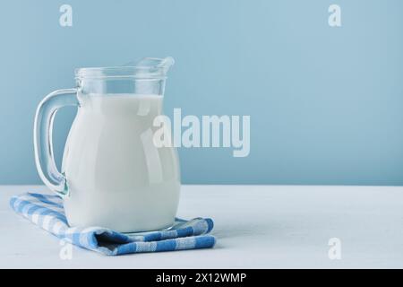 Lait en cruche et verre sur table en bois et fond bleu. Concept de produits laitiers de ferme, journée du lait. Maquette de cuisine ou de supermarché pour le design. Copier s Banque D'Images