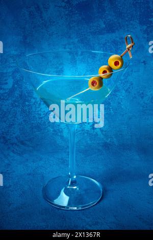 Martini. Un verre de cocktail de martini sale avec vermouth et olives, apéritif, sur fond bleu Banque D'Images