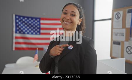 Une femme hispanique souriante montre son autocollant « j'ai voté » dans un centre de vote universitaire avec un drapeau américain en toile de fond Banque D'Images