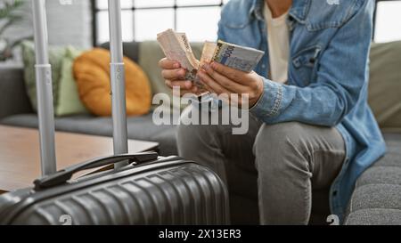 Homme hispanique comptant le coréen gagné avant un voyage, assis à côté des bagages dans un appartement moderne. Banque D'Images