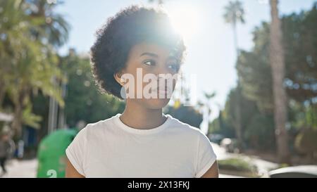 Portrait en plein air d'une femme afro-américaine réfléchie aux cheveux bouclés, regardant loin dans la lumière du soleil. Banque D'Images