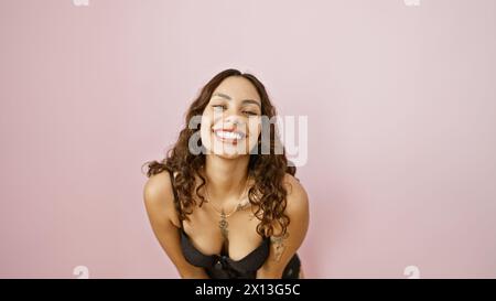 Jeune femme adulte souriante avec les cheveux bouclés, isolée sur un fond rose, respire la confiance et la joie. Banque D'Images