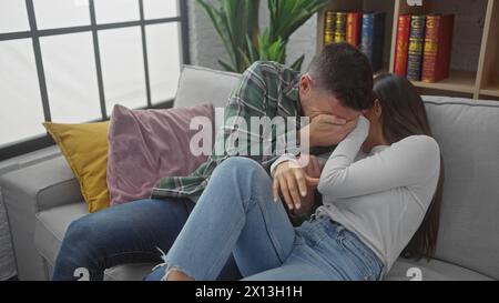 Couple hispanique embrassant dans la tristesse sur un canapé à l'intérieur, montrant le confort et l'émotion. Banque D'Images