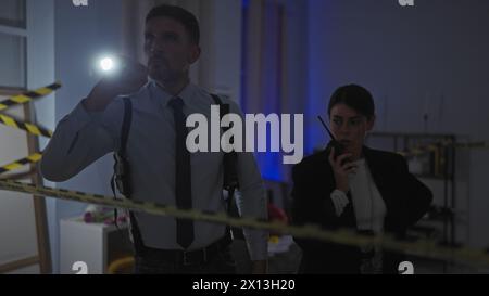 Un homme et une femme enquêtant sur une scène de crime à l'intérieur avec un ruban d'avertissement et des lampes de poche la nuit. Banque D'Images