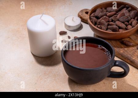 Boisson cérémonielle au cacao. Chocolat cérémonial chaud dans une tasse noire avec des fèves de cacao. Mains de femme tenant une tasse de cacao. Préparation de boisson au chocolat biologique saine Banque D'Images