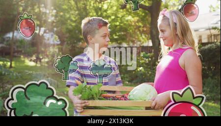 Image des icônes de fruits et légumes sur les frères et sœurs caucasiens heureux avec boîte de légumes Banque D'Images