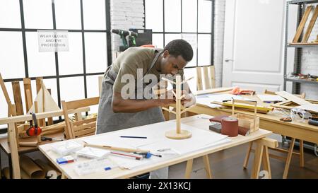 L'homme afro-américain assemble soigneusement le modèle en bois dans un atelier de menuiserie lumineux et organisé. Banque D'Images