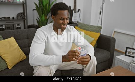 Jeune homme noir souriant comptant des notes de couronnes suédoises dans un salon moderne Banque D'Images