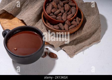Boisson cérémonielle au cacao. Chocolat cérémonial chaud dans une tasse noire avec des fèves de cacao. Mains de femme tenant une tasse de cacao. Préparation de boisson au chocolat biologique saine Banque D'Images