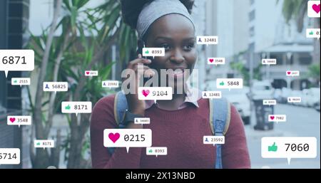 Image de plusieurs icônes de médias sociaux sur une femme afro-américaine parlant sur smartphone à l'extérieur Banque D'Images