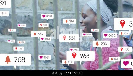 Image de plusieurs icônes de médias sociaux sur une femme afro-américaine utilisant un smartphone à l'extérieur Banque D'Images