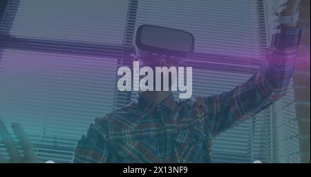 Image de traînées lumineuses bleues et roses se déplaçant au-dessus d'un homme biracial portant un casque vr au bureau Banque D'Images