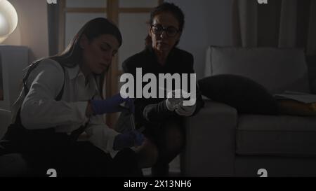 Deux enquêteurs femmes analysent les preuves dans une scène de crime intérieure faiblement éclairée. Banque D'Images