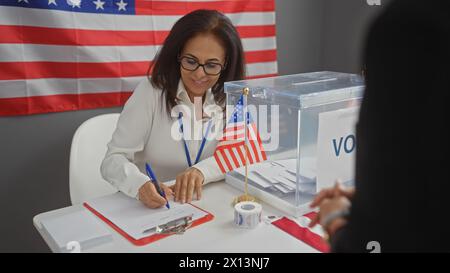 Une femme bénévole dans un collège électoral des états-unis écrit des notes sous un drapeau américain à l'intérieur. Banque D'Images