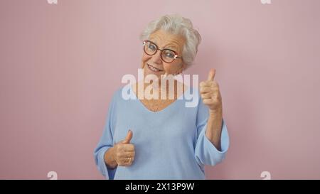 Femme âgée souriante donnant les pouces sur un fond rose, dépeignant la positivité et l'approbation. Banque D'Images