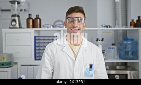 Portrait radieux d'un jeune et beau scientifique hispanique en toute confiance, affichant un sourire gagnant tout en profitant de son travail au laboratoire, portant soigneusement se Banque D'Images