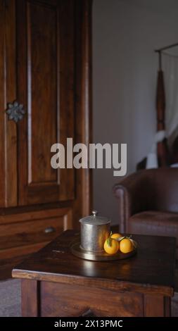 Une théière en étain vintage et des oranges fraîches sur une table en bois élégamment aménagée dans un intérieur confortable et rustique. Banque D'Images