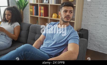 Un jeune couple dans un cadre de salon décontracté, un homme regardant inquiet tandis que la femme est distrait par son téléphone. Banque D'Images