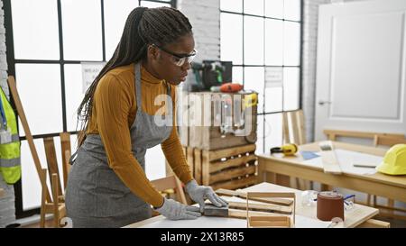 Femme afro-américaine avec des tresses travaillant dans un atelier de menuiserie à l'intérieur Banque D'Images