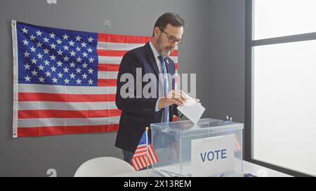 Un homme d'âge moyen qui vote dans un collège électoral américain avec un drapeau en toile de fond. Banque D'Images