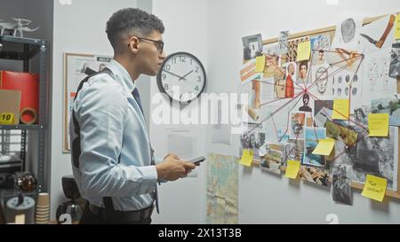 Un jeune homme analyse un comité criminel avec des photos et des notes dans le bureau d'un détective à l'intérieur. Banque D'Images