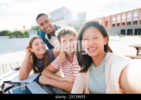 Un groupe d'adolescents heureux et divers souriants, prenant un portrait selfie ensemble lors d'un rassemblement d'étudiants. De jeunes amis de diverses origines ethniques rient et capturent le moment avec un smartphone. Photo de haute qualité Banque D'Images