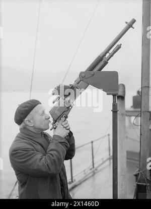 YACHT D'INSTRUCTION DEMS MOBILE. 23 FÉVRIER 1942, À BORD DU MY MELITA, BAIE DE GOUROCK. LE LANCEMENT MOTORISÉ EST LE PREMIER LANCEMENT INSTRUCTIF À ÊTRE UTILISÉ POUR L'ÉQUIPEMENT DÉFENSIF DES NAVIRES MARCHANDS AU ROYAUME-UNI. IL EFFECTUE DES TRAJETS QUOTIDIENS JUSQU'AUX MOUILLAGES POUR TENIR LES MARINS MARCHANDS INFORMÉS ET INSTRUITS DES DERNIÈRES AMÉLIORATIONS POUR LA DÉFENSE DE LEURS NAVIRES. - AB Moy Jones, 68 ans, pilote la mitrailleuse Hotchkiss à bord de MELITA Banque D'Images